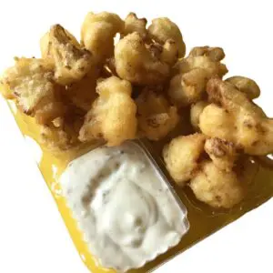 Fried popcorn chicken with dipping sauce on a yellow tray.