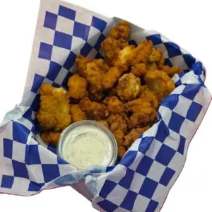 Basket of fried popcorn chicken with dipping sauce on checkered paper.