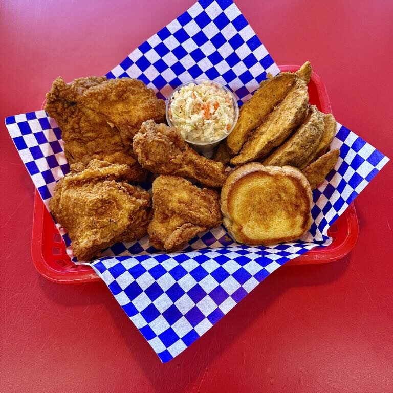 A basket of fried chicken with sides on checkered paper.