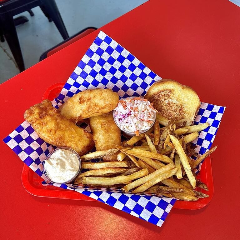 Fried chicken, fries, onion rings, and dipping sauces on a checkered paper.